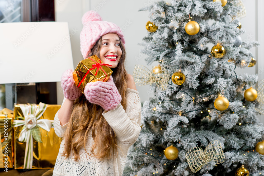 Young smiling woman in knitted hat and gloves holding a gift box celebrating winter holidays in the 