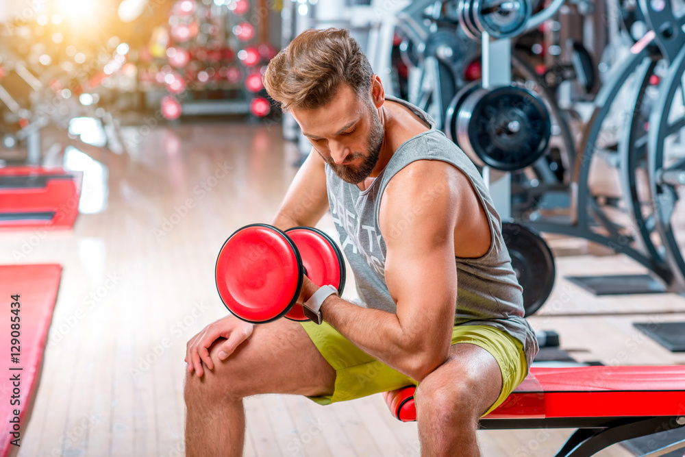 Muscular man training with red dumbbell in the gym