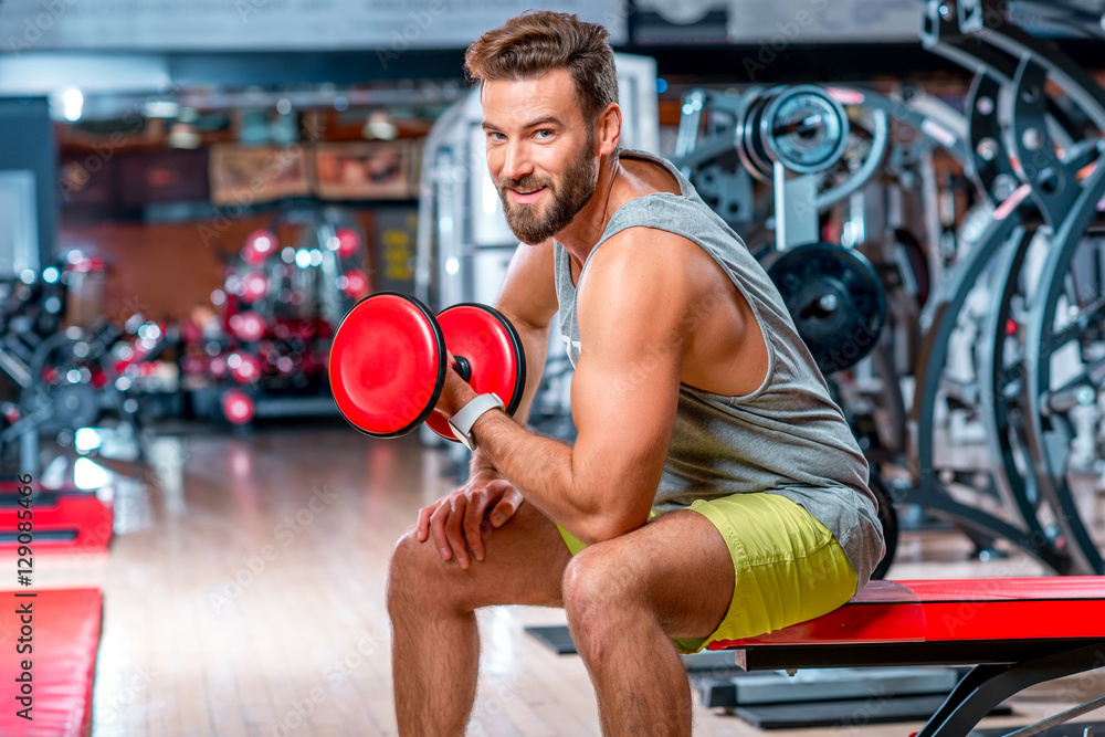 Muscular man training with red dumbbell in the gym