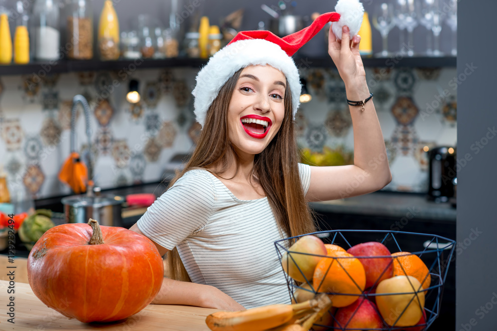 Portrait of a young smiling woman in the Christmas hat in the kitchen at home