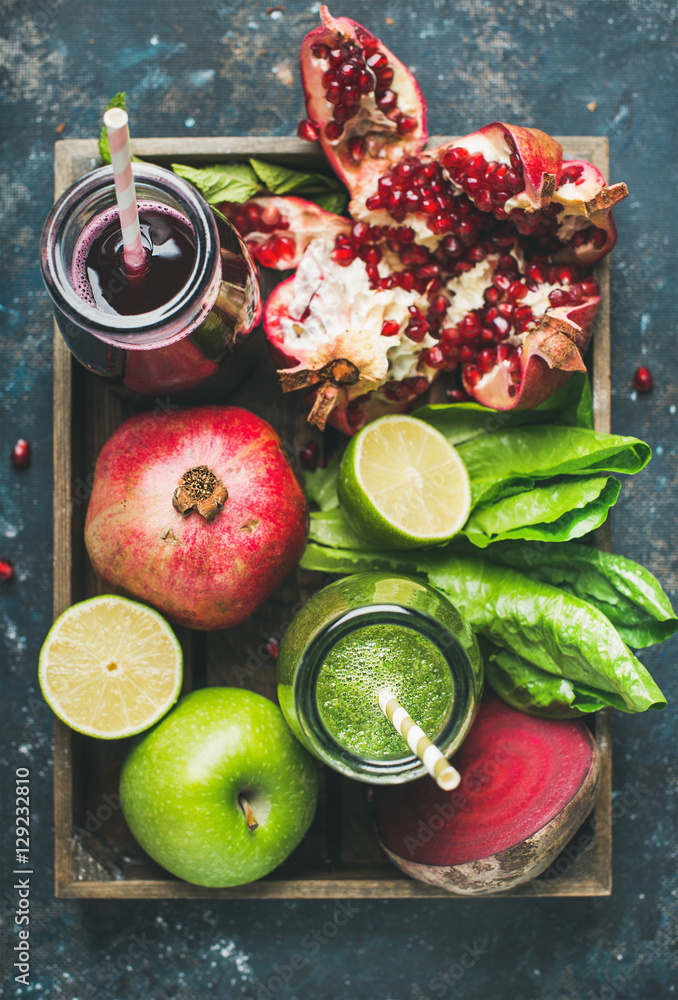 Green and purple fresh juices or smoothies with fruit, greens, vegetables in wooden tray over dark b