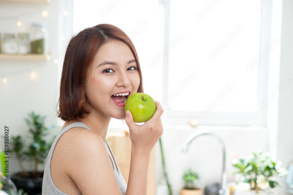 快乐的年轻亚洲女人在厨房里吃绿苹果。节食。死亡