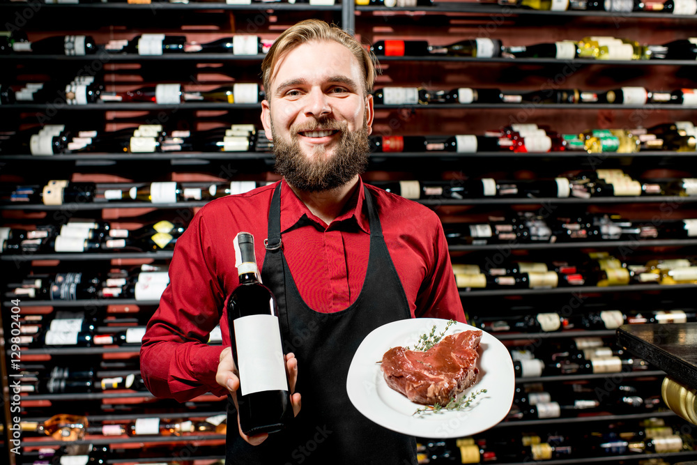 Portrait of a seller or sommelier with wine bottle and steak on the plate at the luxury supermarket 