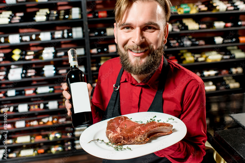 Portrait of a seller or sommelier with wine bottle and steak on the plate at the luxury supermarket 