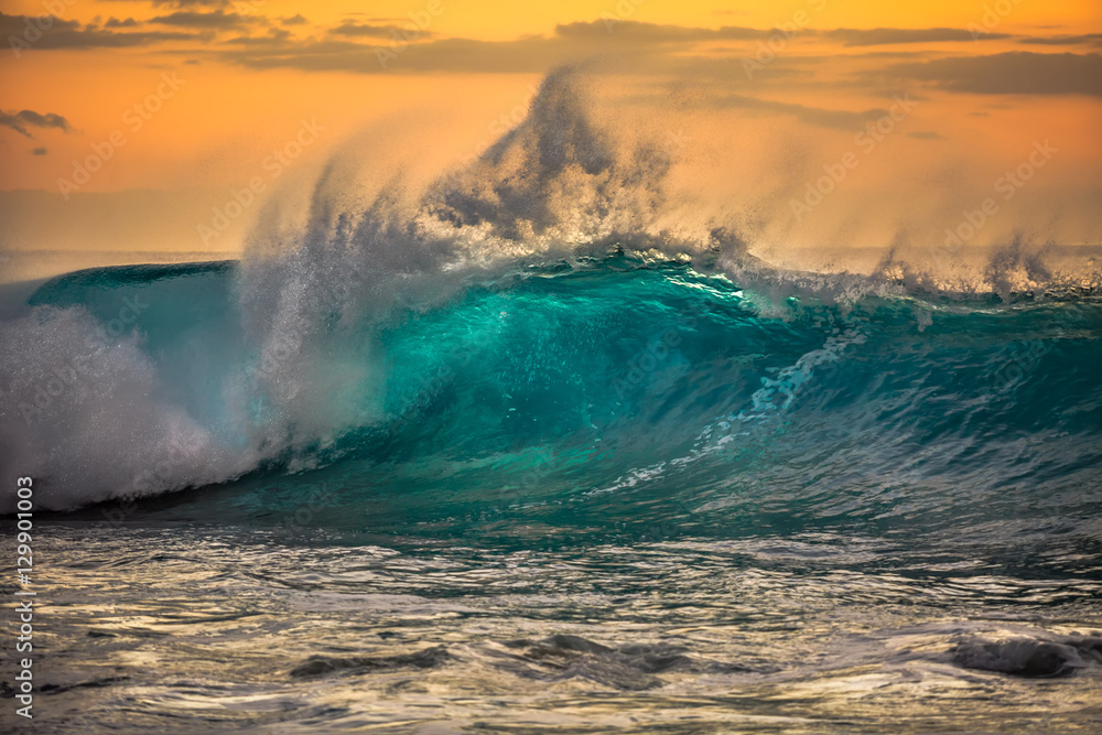 Green blue ocean splashing wave in front of orange sunset sky background