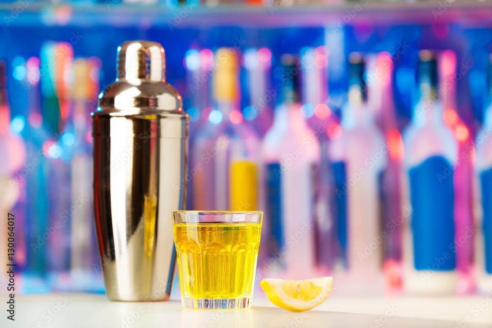 Glass with cocktail, lemon and shaker on a counter