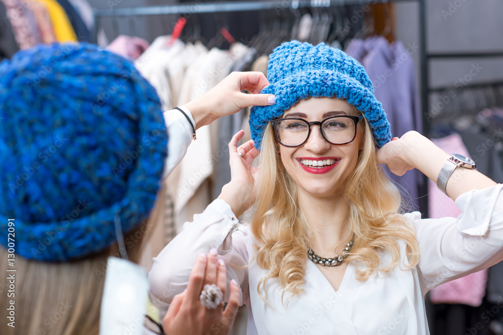 Two beautiful women trying blue hats in the clothing store. Happy winter shopping