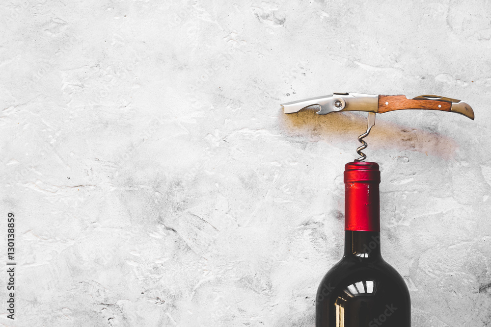 glass wine bottle and corkscrew on concrete background top view