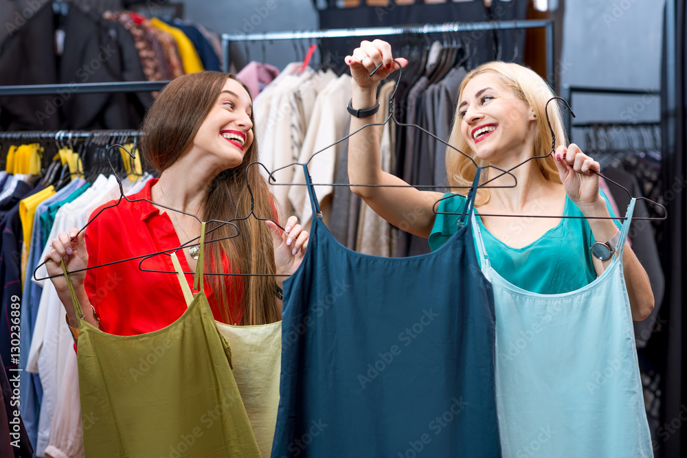 Beautiful women choosing shirts in the clothing store. Female friends having fun shopping in the bou