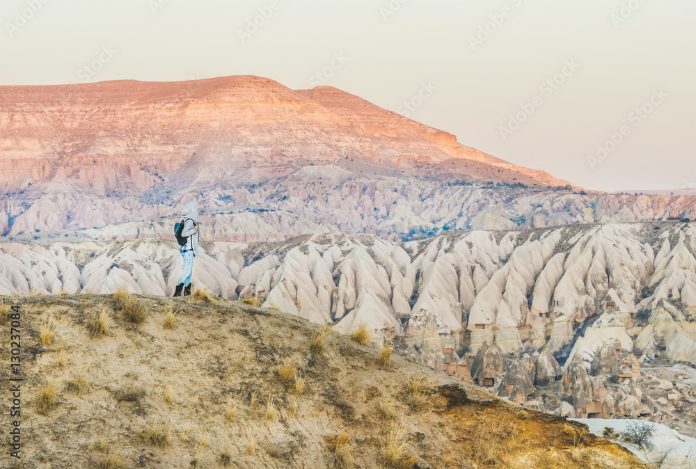 Young woman traveller looking aside and hiking in the mountains among natural rocks of Cappadocia, C