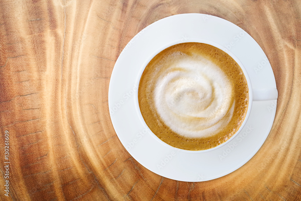 Top view of hot coffee cappuccino latte cup with saucer on wood table texture background.