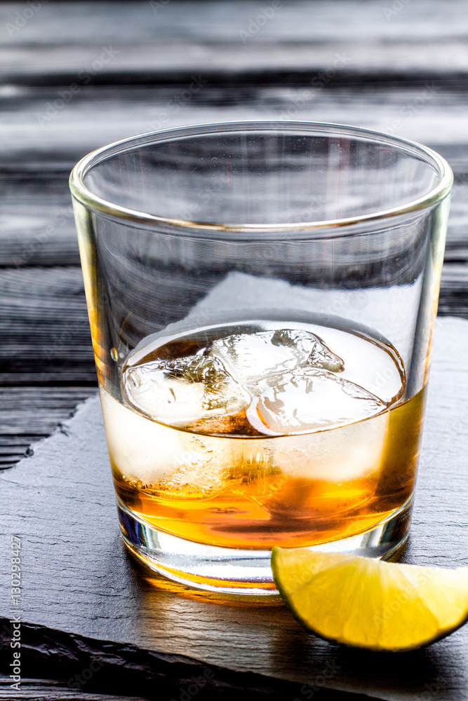 rum with ice in glass on dark background and lime