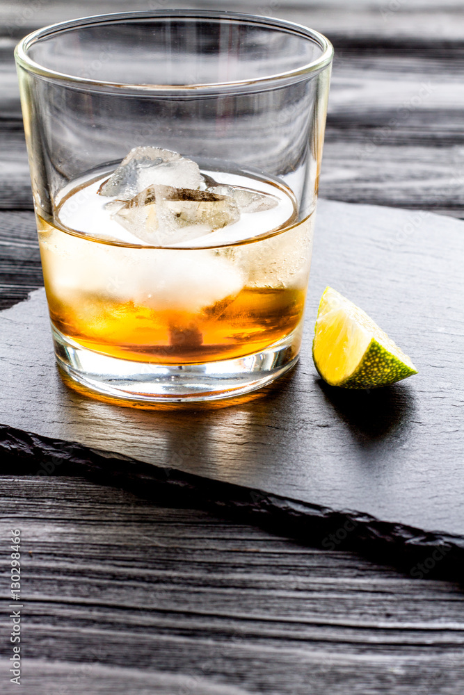 rum with ice in glass on dark background and lime