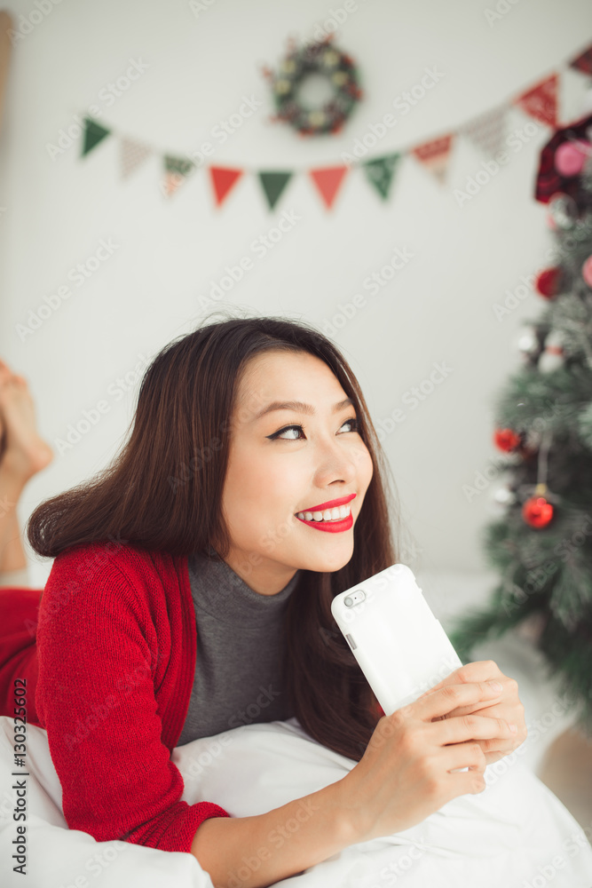 年轻微笑的亚洲女人在用手机。圣诞节和N