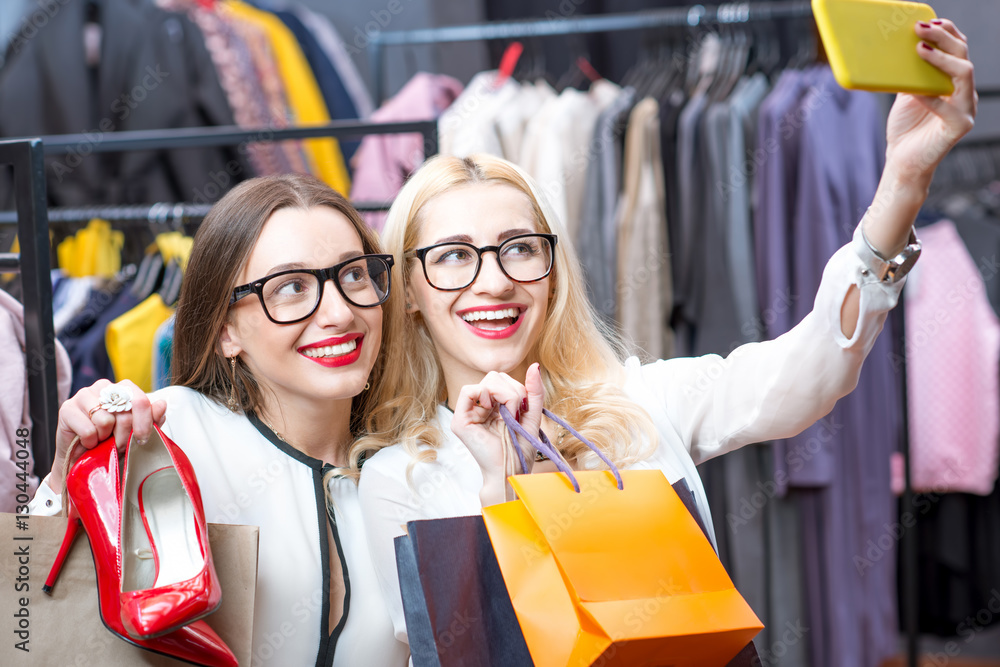 Two happy businesswomen making selfie portrait with shopping bags and shoes in the luxury clothing s