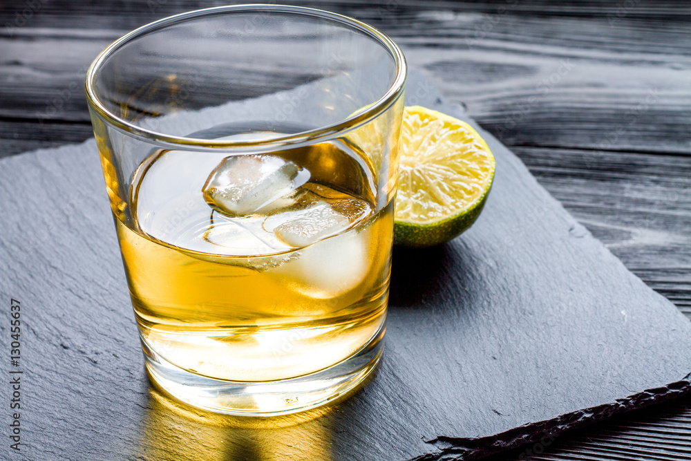 rum with ice in glass on dark background and lime