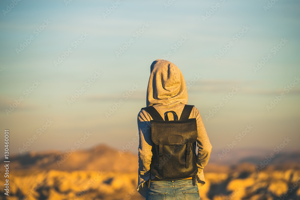 Young woman traveller wearing hoodie and backpack watching sunrise in the mountains over Goreme, Cap