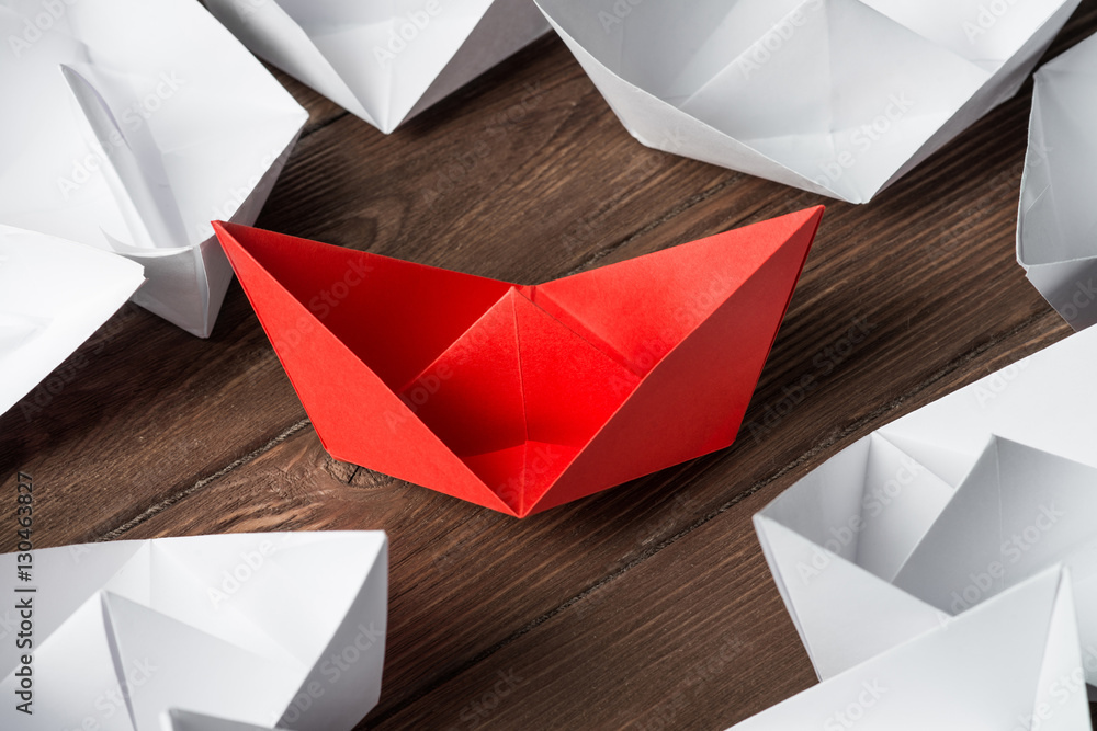 Business leadership concept with white and color paper boats on wooden table