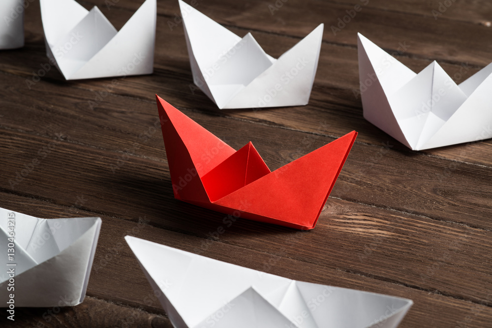 Business leadership concept with white and color paper boats on wooden table