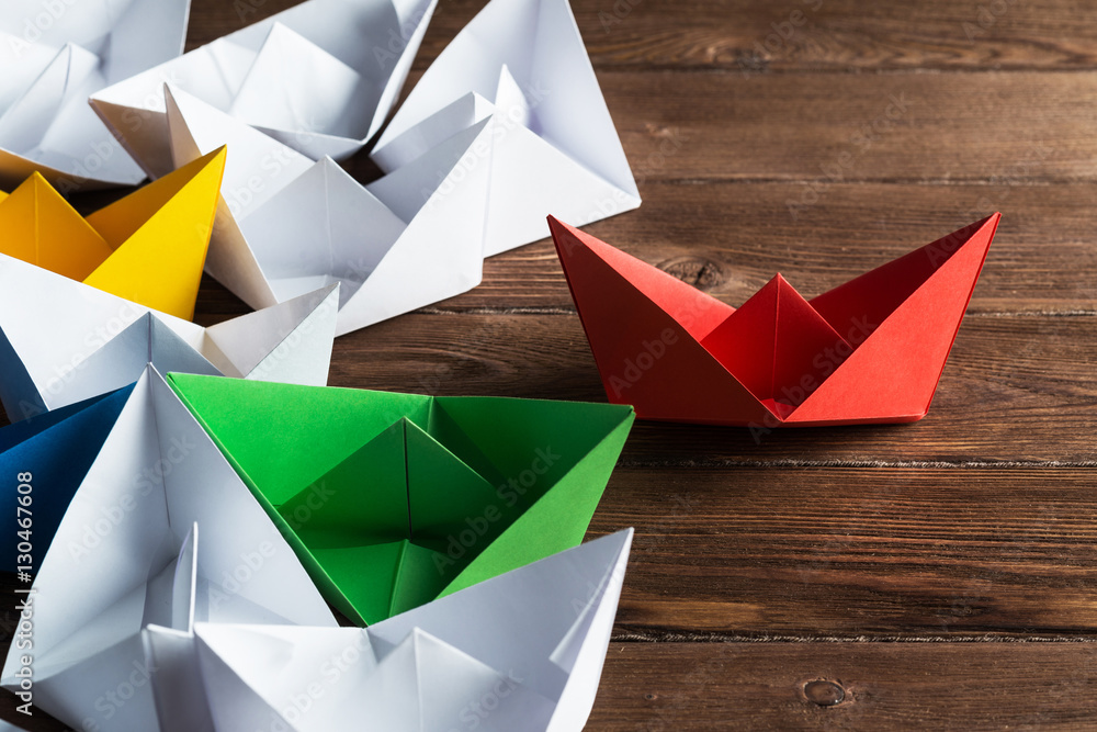 Business leadership concept with white and color paper boats on wooden table