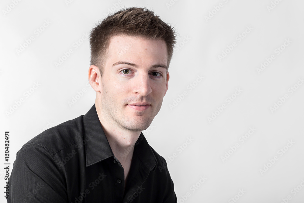 Handsome young man in a black shirt leaning against a light gray