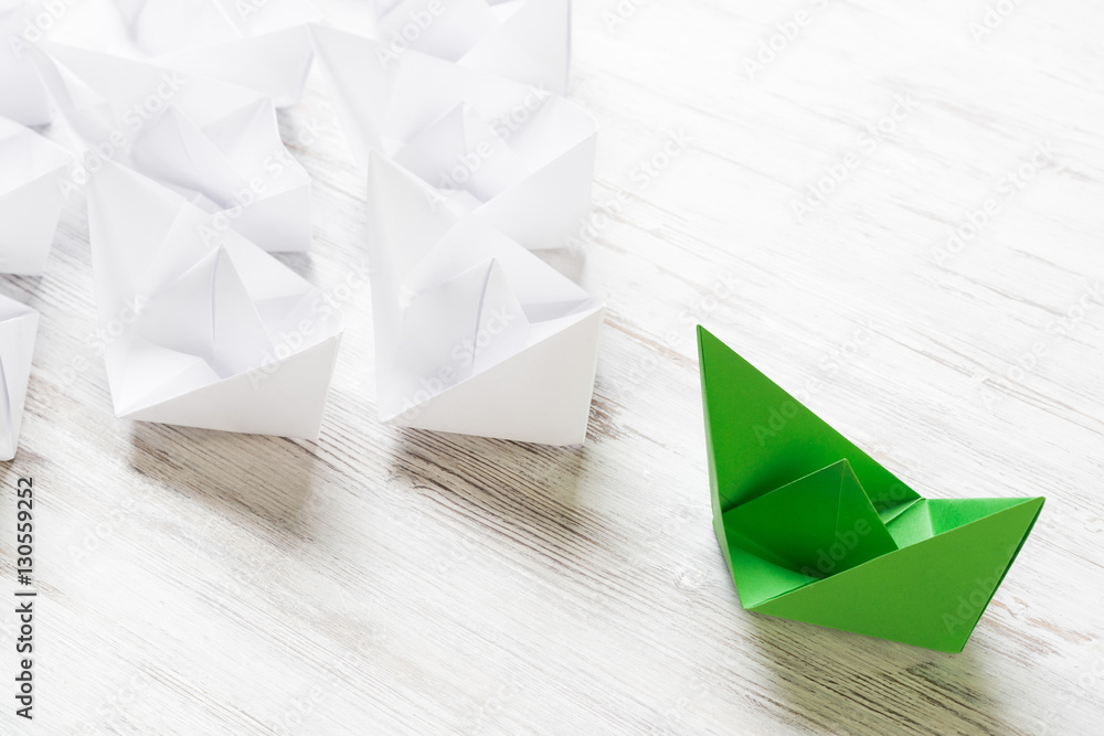 Business leadership concept with white and color paper boats on wooden table