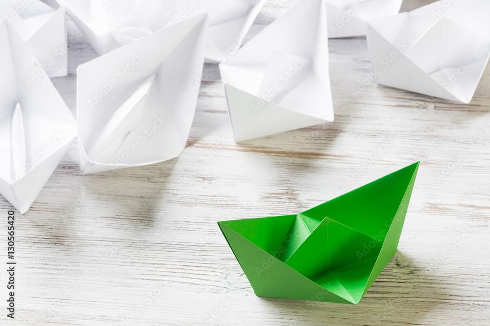 Business leadership concept with white and color paper boats on wooden table