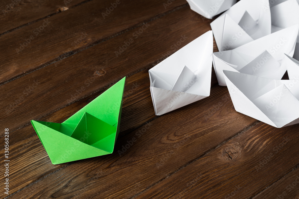 Business leadership concept with white and color paper boats on wooden table