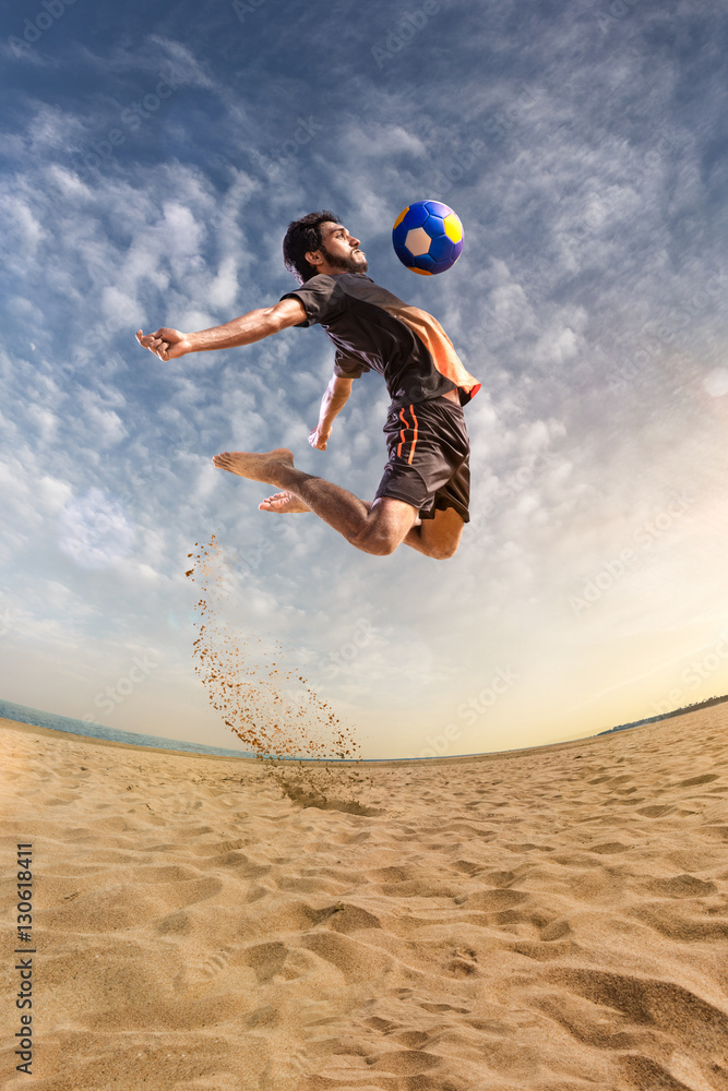 Beach soccer player in action. Sunny beach wide angle and sea