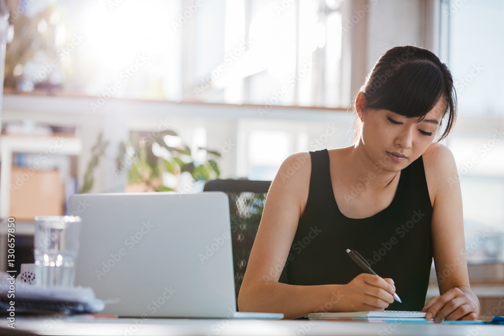 Young woman sitting at desk and writing notes