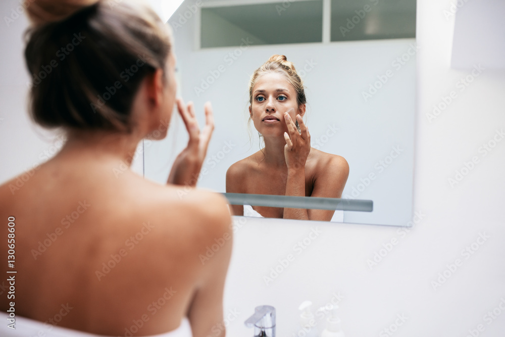 Woman in bathroom applying cream on face