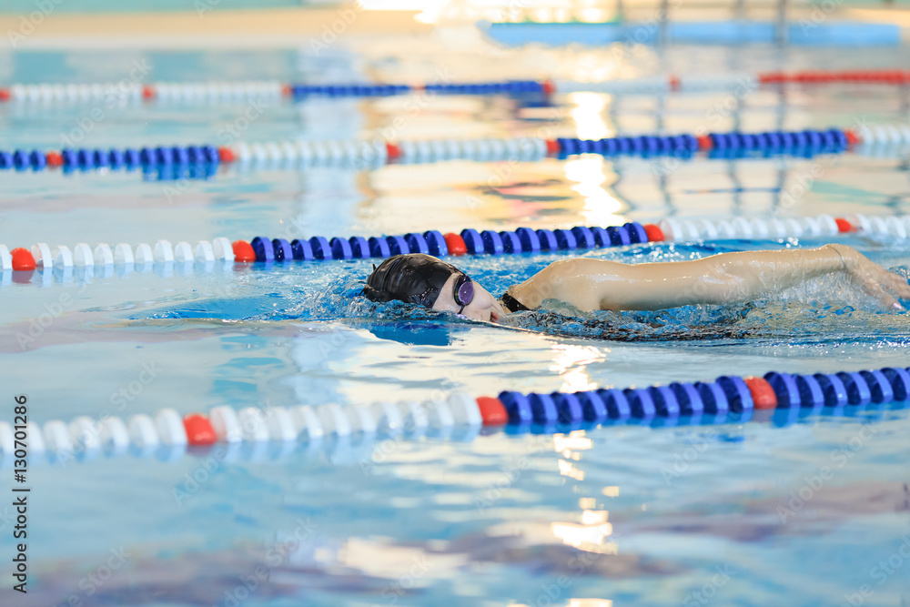 Young woman in goggles and cap swimming front crawl stroke style in the blue water indoor race pool.