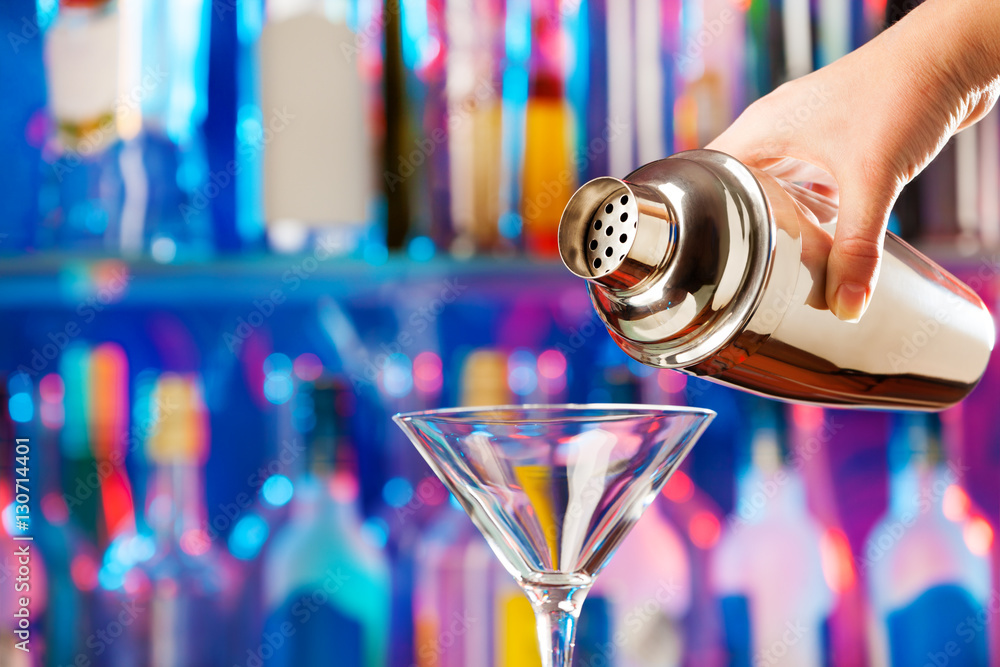 Barman hand pouring drink  into a cocktail glass