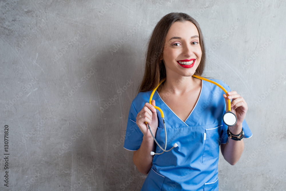 Portrait of a young nurse in uniform with stethoscope on the gray wall background