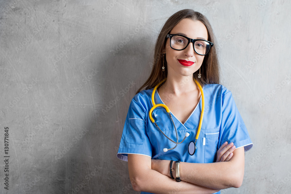 Portrait of a young nurse in uniform with stethoscope on the gray wall background