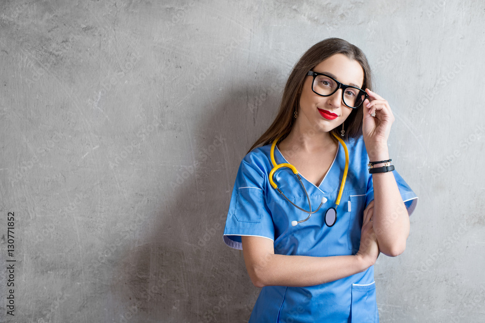 Portrait of a young nurse in uniform with stethoscope on the gray wall background