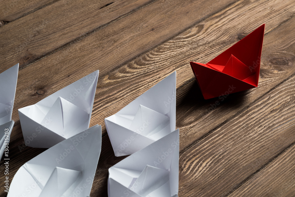 Business leadership concept with white and color paper boats on wooden table