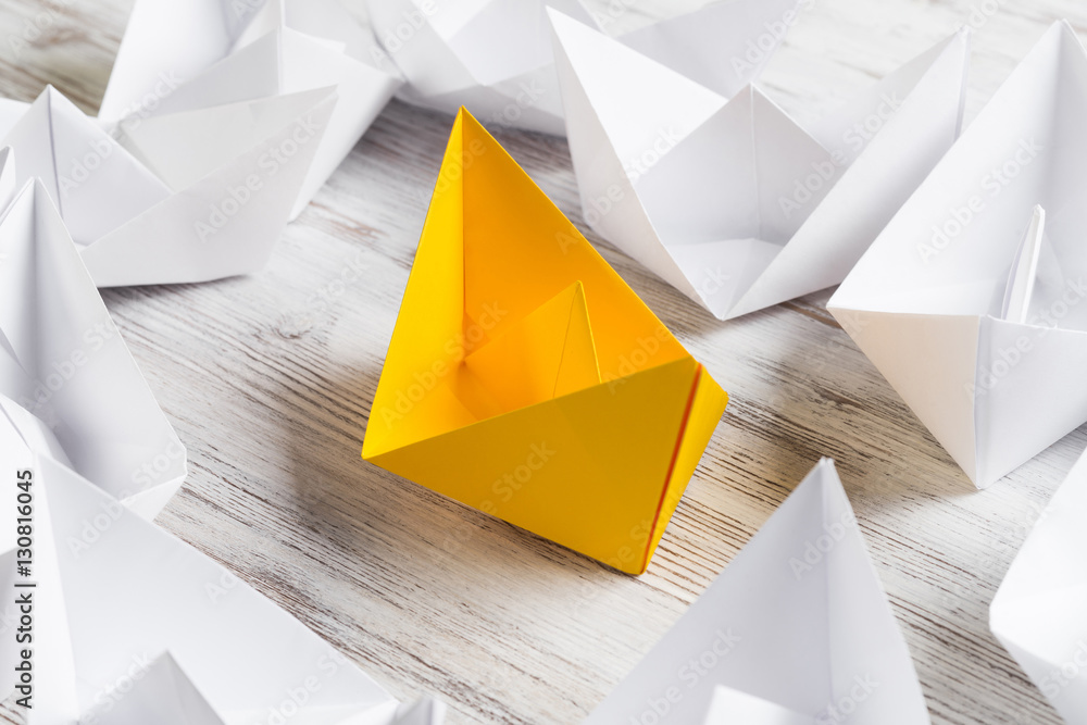 Business leadership concept with white and color paper boats on wooden table