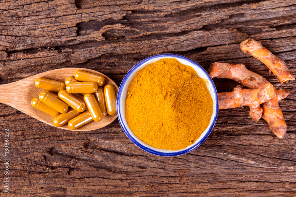 the turmeric powder , capsule and roots curcumin on wooden plate