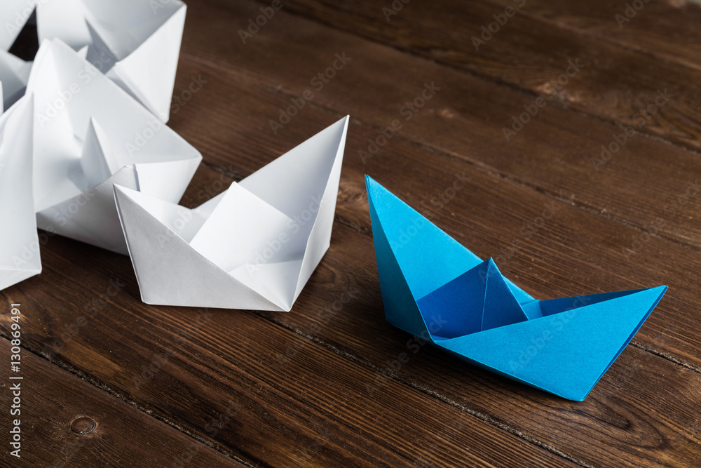 Business leadership concept with white and color paper boats on wooden table