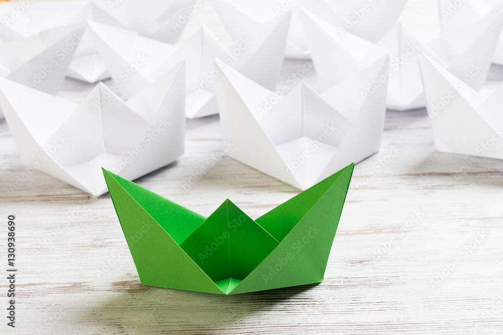 Business leadership concept with white and color paper boats on wooden table