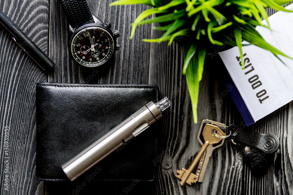 leather wallet, watch, electronic cigarette dark wooden background top view