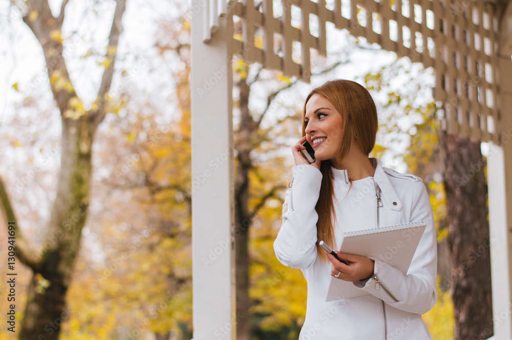 Beautiful young woman talking on a phone in city park.