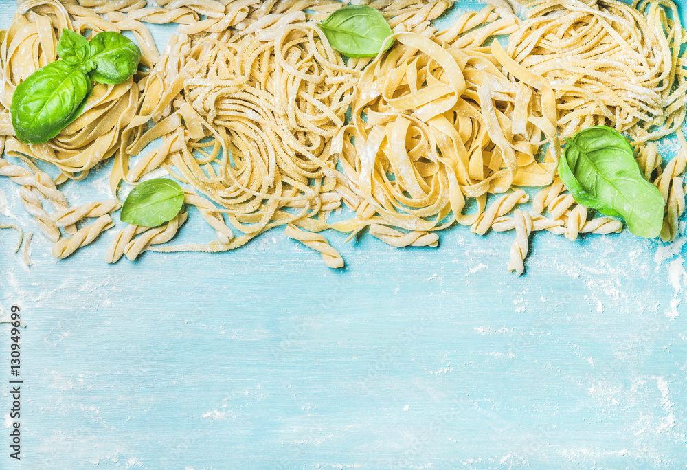 Various homemade fresh uncooked Italian pasta with flour and green basil leaves on blue wooden backg