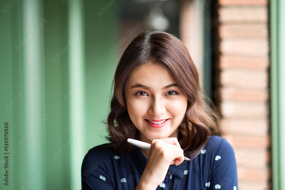 Young beautiful woman in the cafe near the window, thinking and writing something.