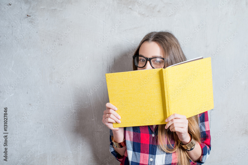 Portrait of a young happy student in checkered shirt with yellow book on the gray wall background