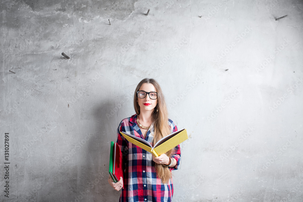 Portrait of a young student in checkered shirt with yellow book on the gray wall background. Image w