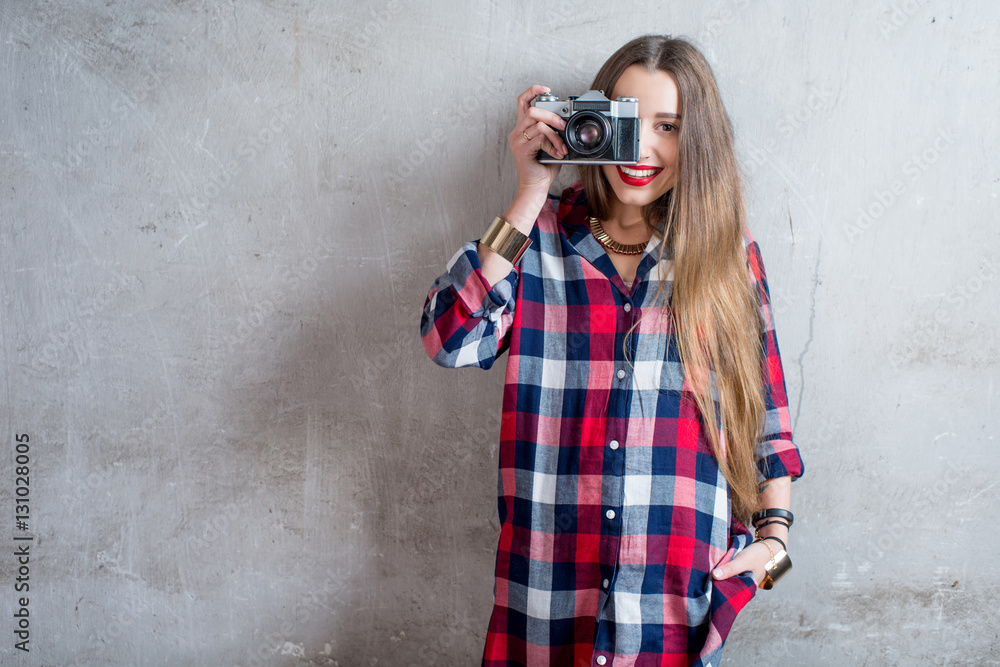 Portrait of young female photographer with retro camera on the gray wall background