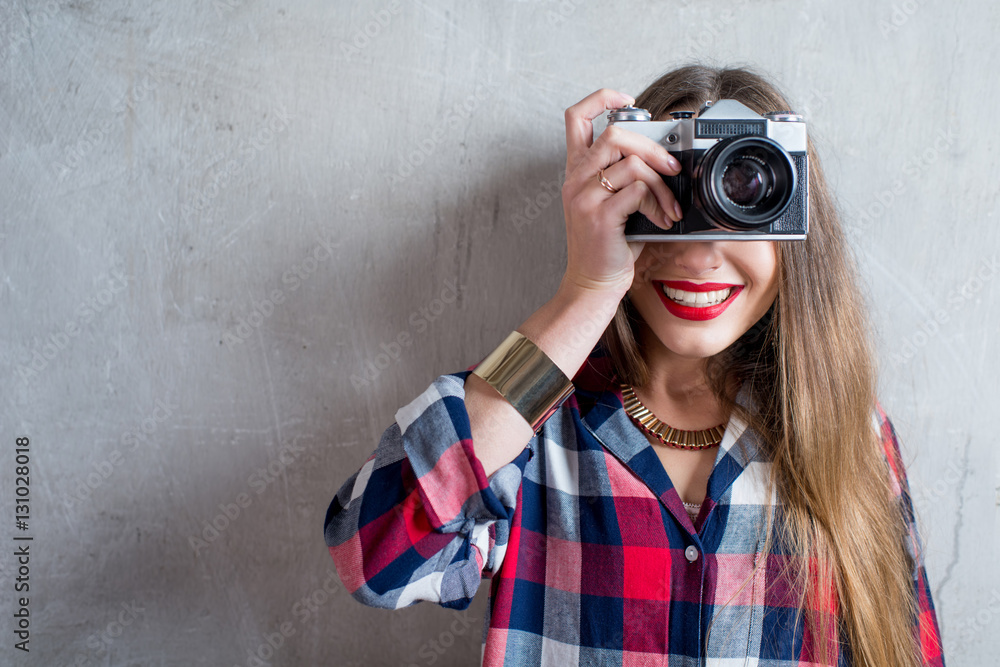 Portrait of young female photographer with retro camera on the gray wall background