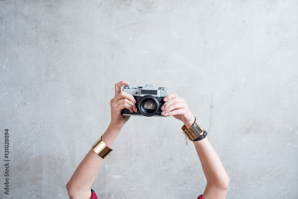 Female hands holding retro photo camera on the gray wall background